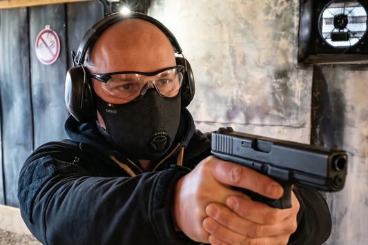 Un homme pratiquant le tir sportif, visant avec son arme, tout en portant des lunettes, un casque anti bruit ainsi qu'un masque de tir sportif