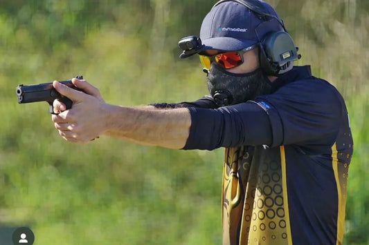 Un homme pratiquant le tir sportif avec une arme à la main, des lunettes, un casque anti-bruit ainsi qu'un masque pour le tir sportif