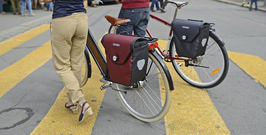 deux personnes qui poussent leur vélo avec des sacoches à l'arrière