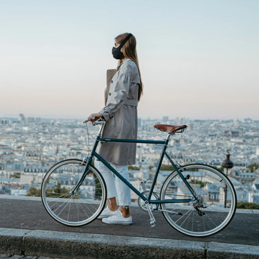 Femme avec une masque anti-pollution, un vélo avec une ville en arrière plan.
