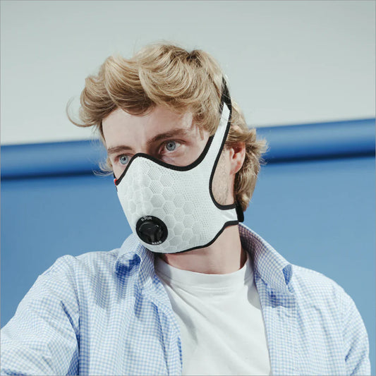 Un homme vêtu d'un tee-shirt blanc, une chemise bleu ouverte et un masque anti allergie blanc. 