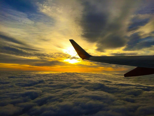 Aile d'avion dans le ciel avec le soleil au dessus des nuages.