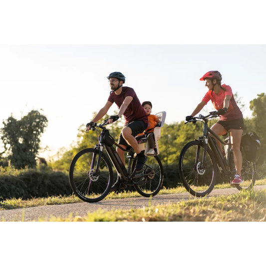 Un couple sur deux vélos électriques en ballade avec un enfant sur un siège-bébé de vélo