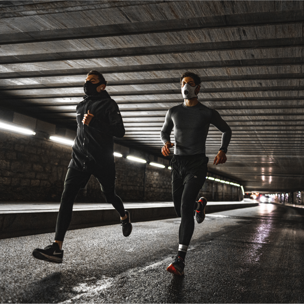 Two runners moving through a city tunnel while wearing running pollution masks.