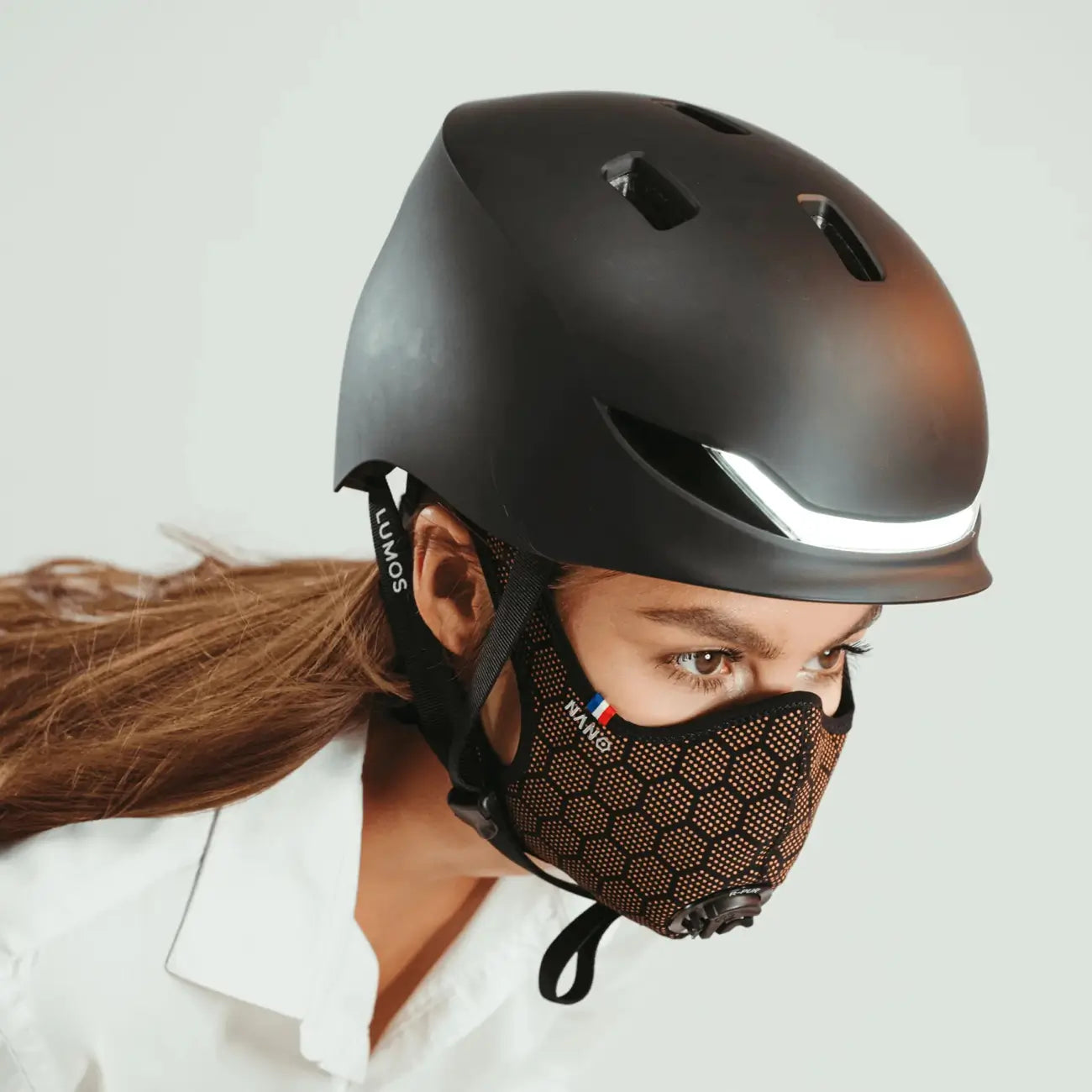 Cyclist on the road looking back, wearing a orange R-PUR mask, black helmet with a light.