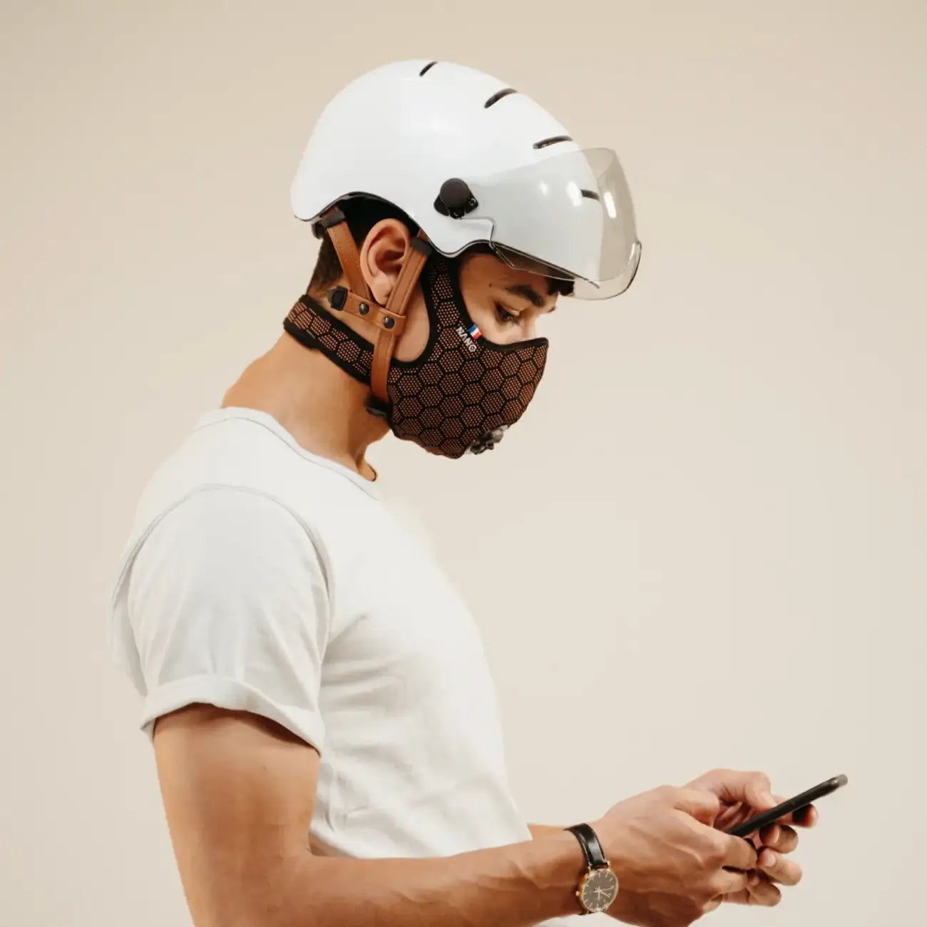 Cyclist wearing a orange R-PUR cycling mask and white helmet, looking to his phone.