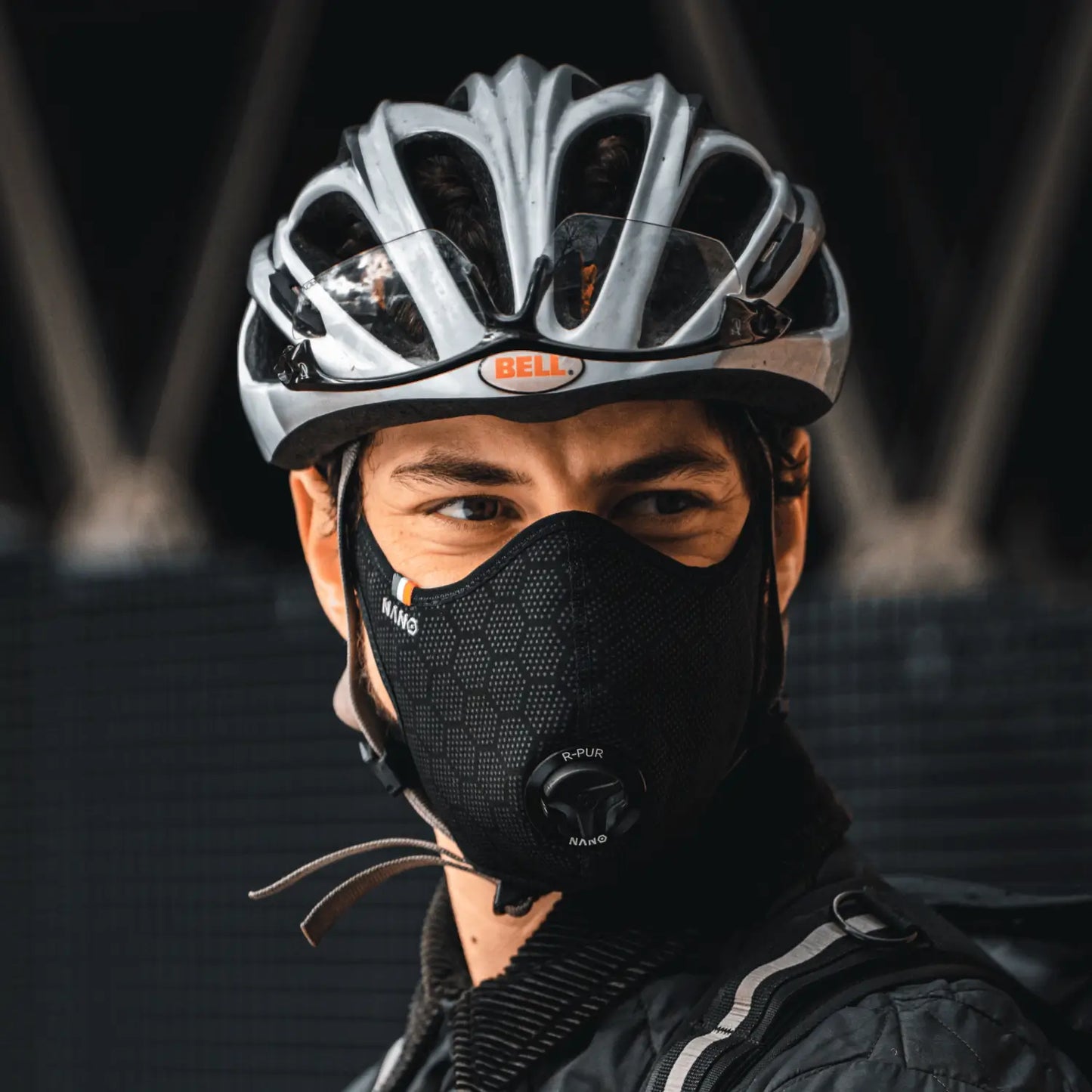 Cyclist wearing a black R-PUR cycling mask and silver helmet, looking to the side.