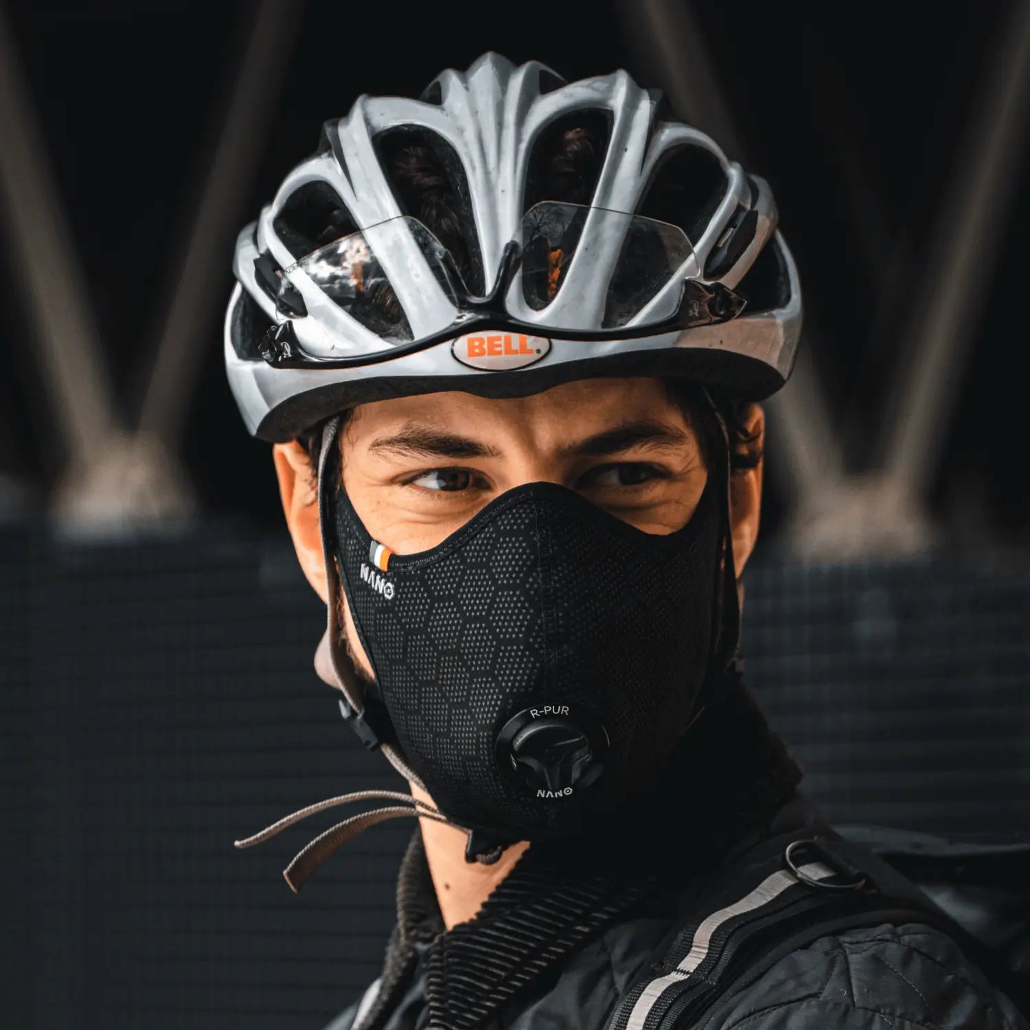 Cyclist wearing a black R-PUR cycling mask and silver helmet, looking to the side.