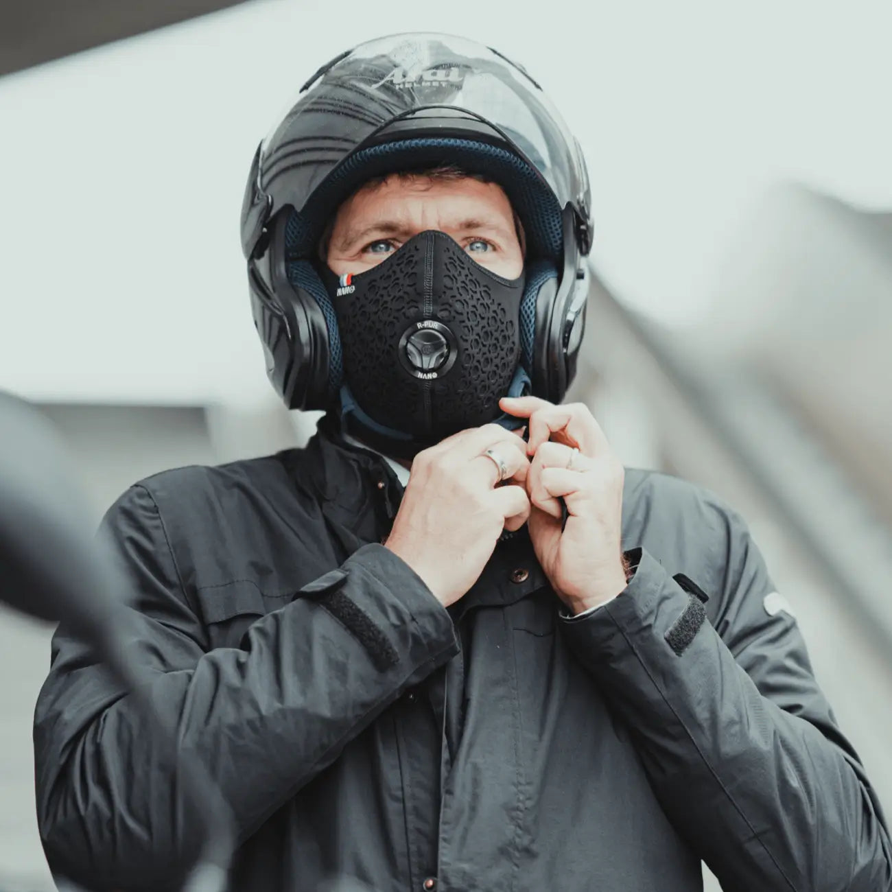 Rider in a motorcycle helmet tightening the strap, wearing a black motorcycle R-PUR mask