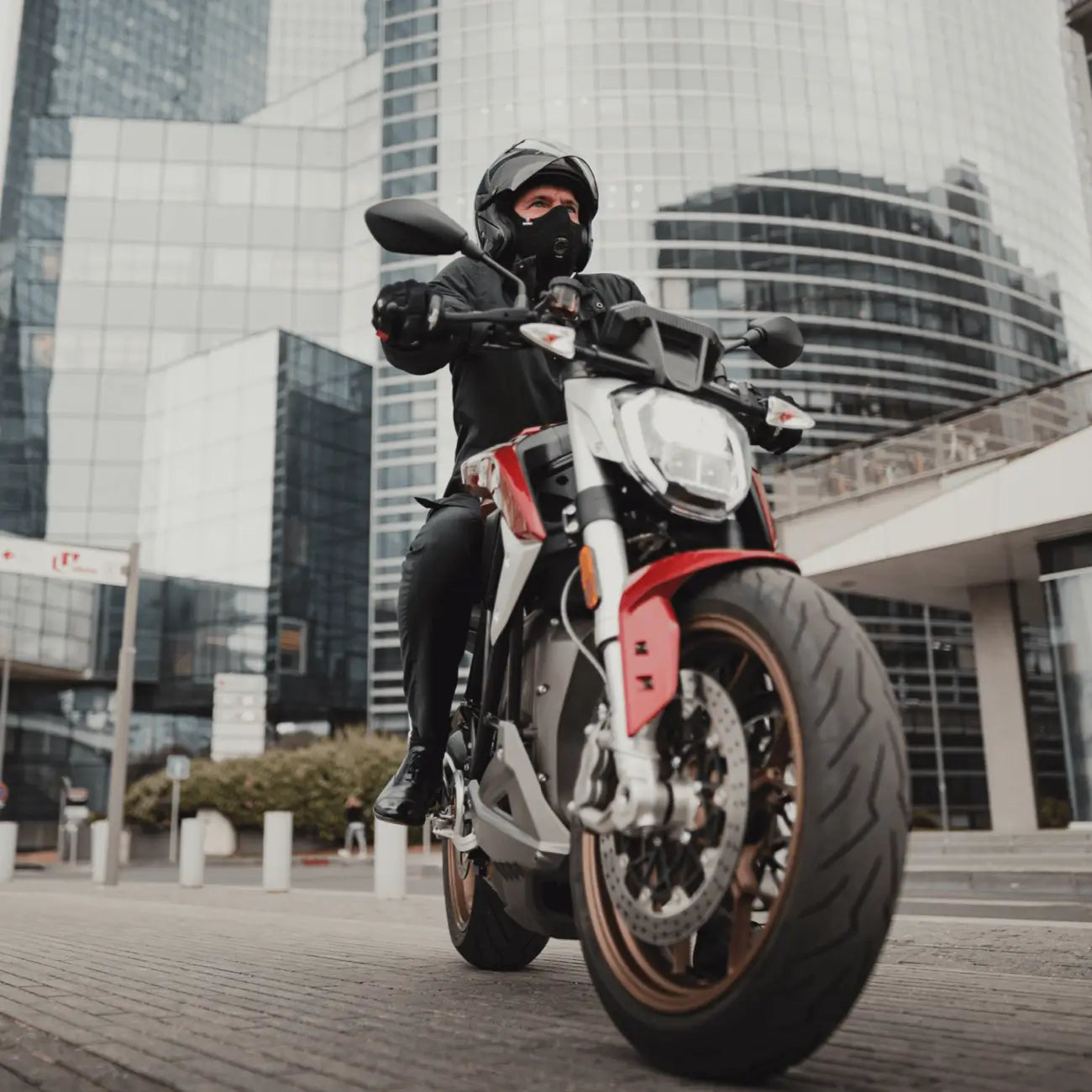 Motorcyclist wearing an R-PUR Nano one mask rides a red-and-silver bike in a modern city