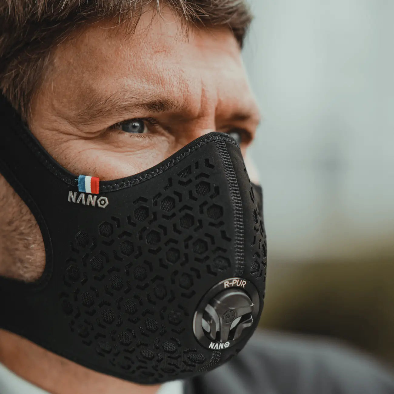 Side view of a rider wearing a black R-PUR motorcycle mask with hex pattern and front valve